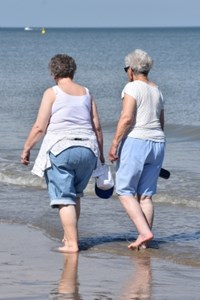 Two older women walking barefoot along a beach.